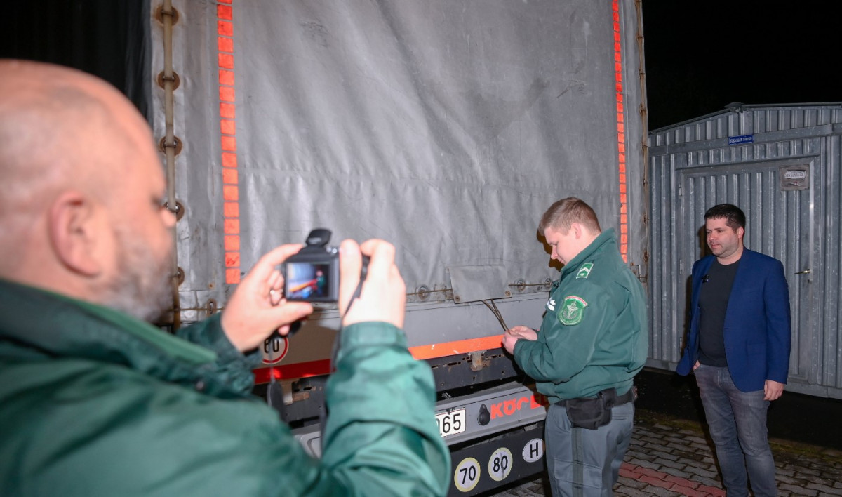 A NAV szakemberei plombát raknak egy Ukrajna felől érkezett tranzitkamionra, miután mintát vettek a Nemzeti Élelmiszerlánc-biztonsági Hivatal (Nébih) szakemberei a jármű kukoricaszállítmányából a záhonyi közúti határátkelőhelyen 2023. április 17-én késő este. Jobbra, Nobilis Márton, az Agrárminisztérium élelmiszeriparért és kereskedelempolitikáért felelős államtitkára.